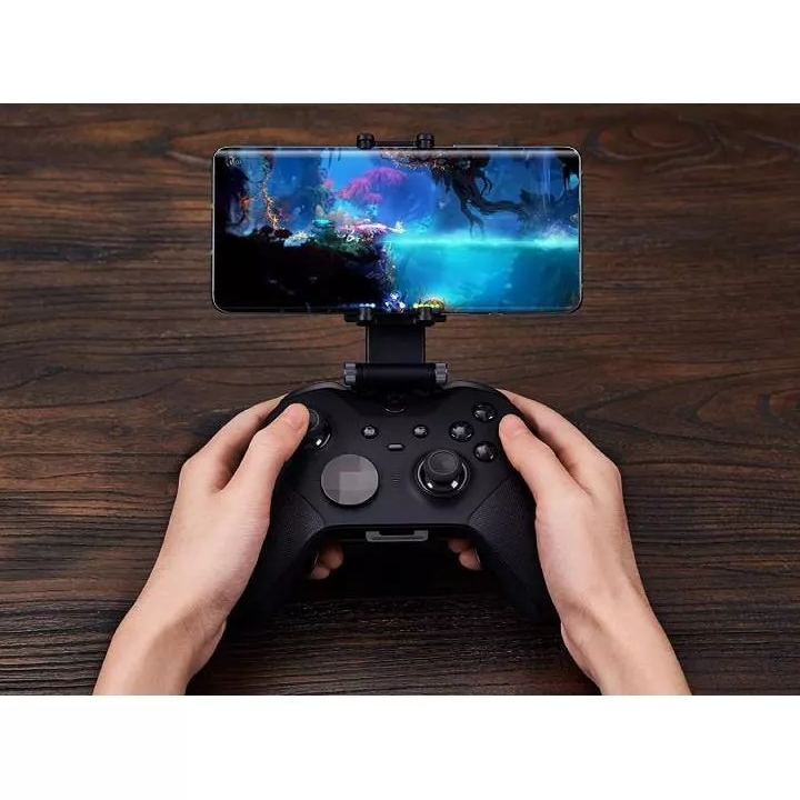 Un téléphone est accroché à une manette de XBOX via le support de téléphone 8BitDo. Deux mains tiennent cette manette.